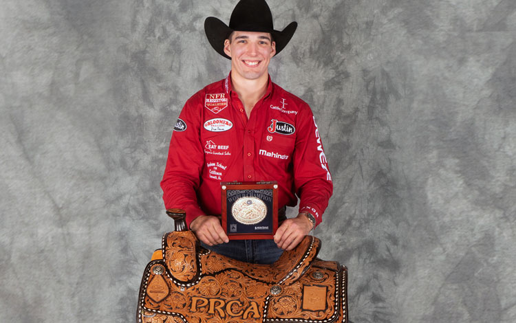 Jess Pope posing and standing behind his world champion saddle and holding his gold buckle